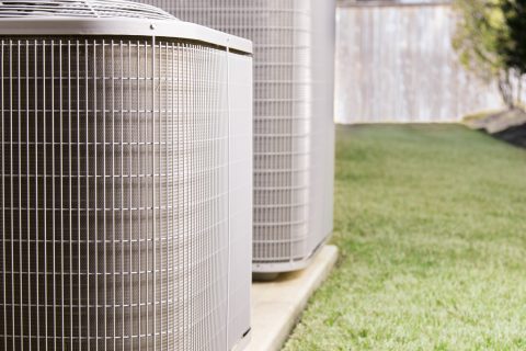 Two air conditioner units outside a large brick home.