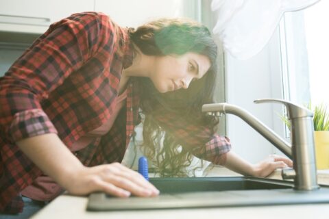 Woman Checking Kitchen Faucet For Leaks