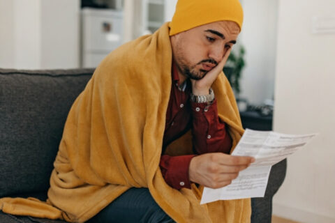 Cold & Upset Man sitting on a sofa with a Heating bill