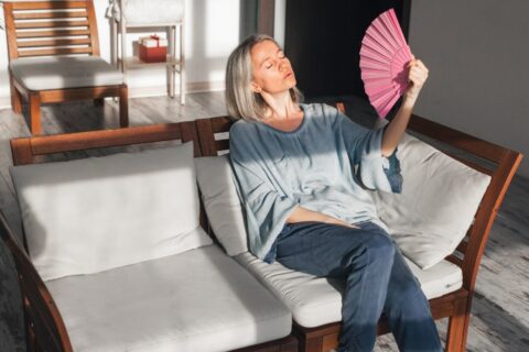 Exhausted middle aged woman using paper waver, suffering from AC shut down