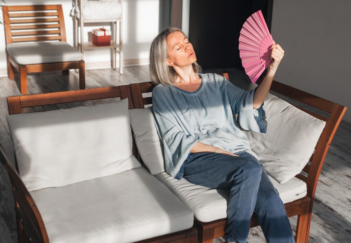 Exhausted middle aged woman using paper waver, suffering from AC shut down